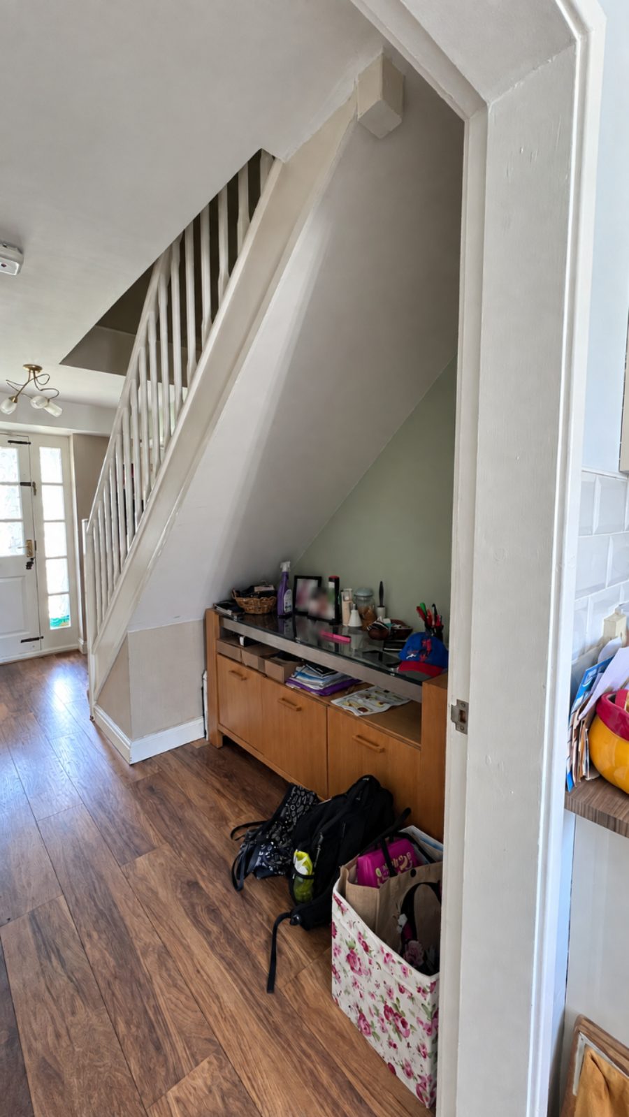 Before: the open space under the stairs with a sideboard and bags on the floor, and a white-spindled balustrade